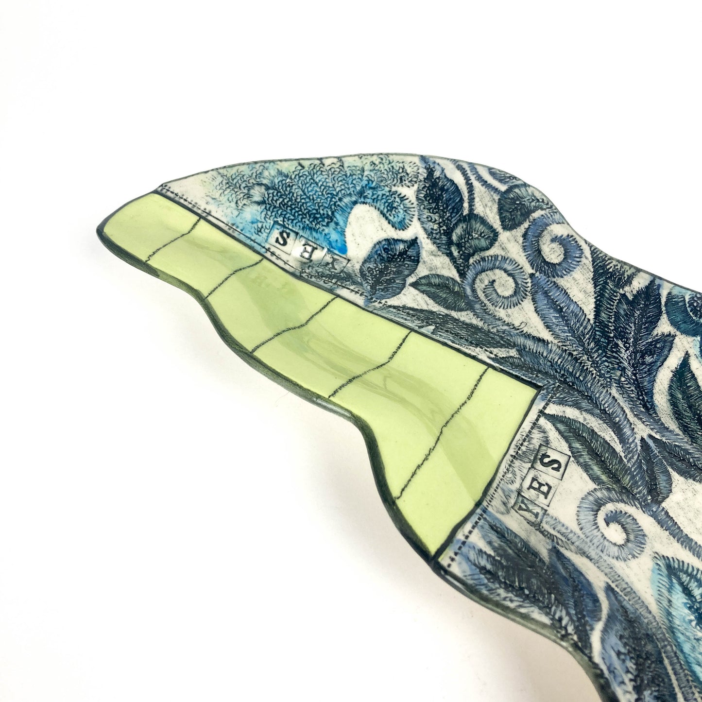 Underside of the Peapod Platter showing a wavy shape, dotted glaze, and artist’s signature stamp.