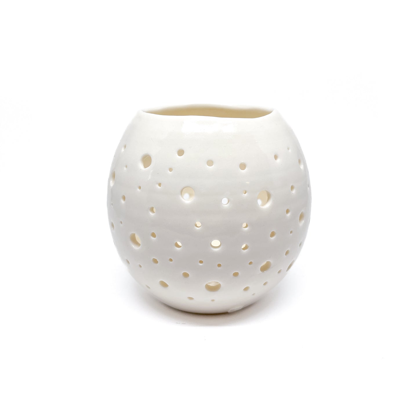 A round, white ceramic tealight holder with small holes cut out around its surface.