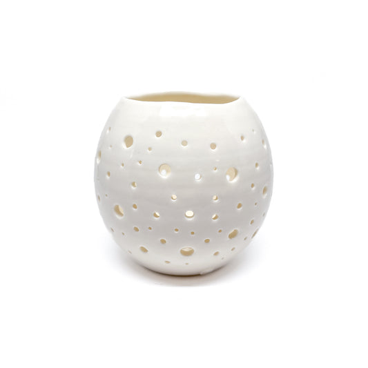 A round, white ceramic tealight holder with small holes cut out around its surface.