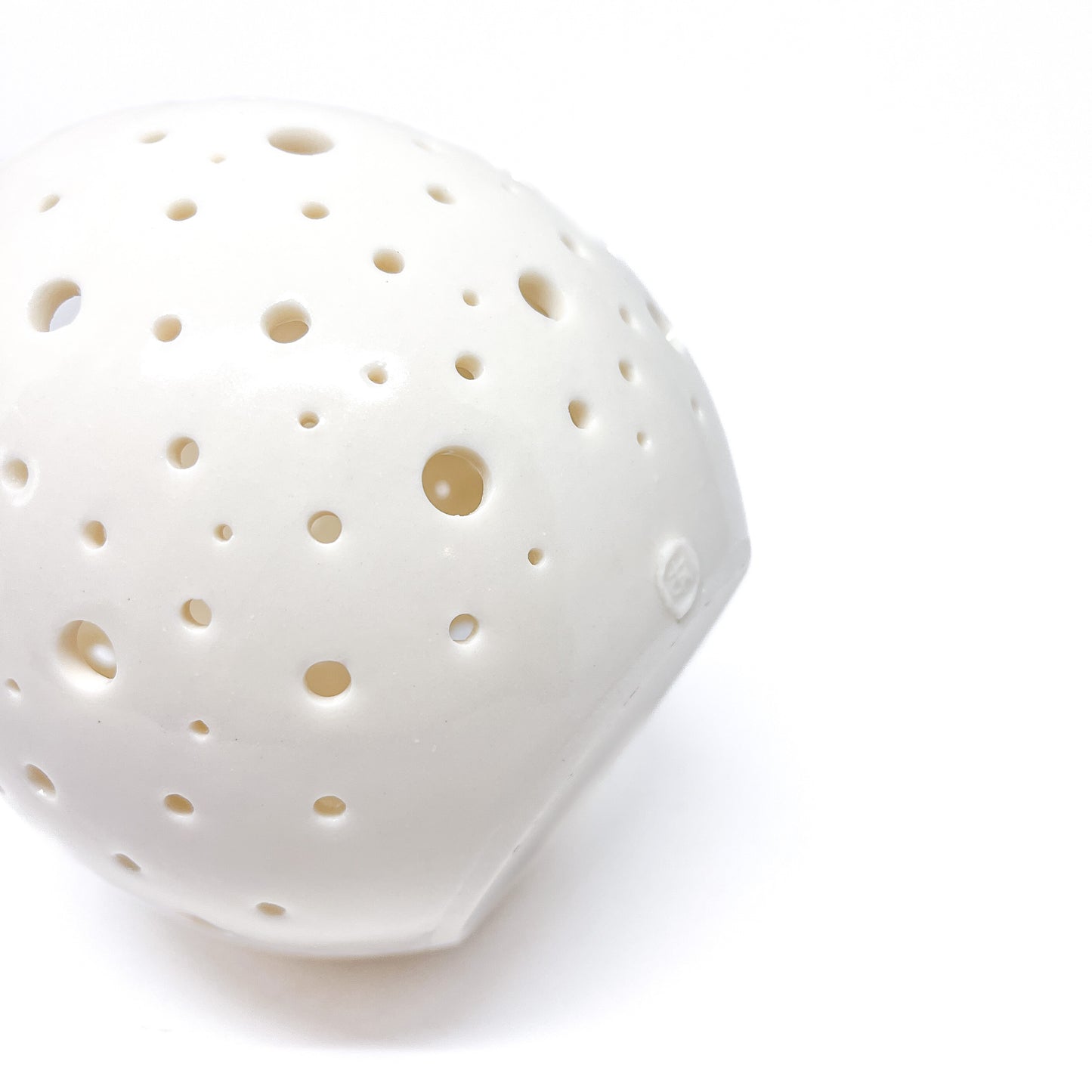 A close-up of a white ceramic tealight holder with small holes cut out around its surface, seen from a low angle.