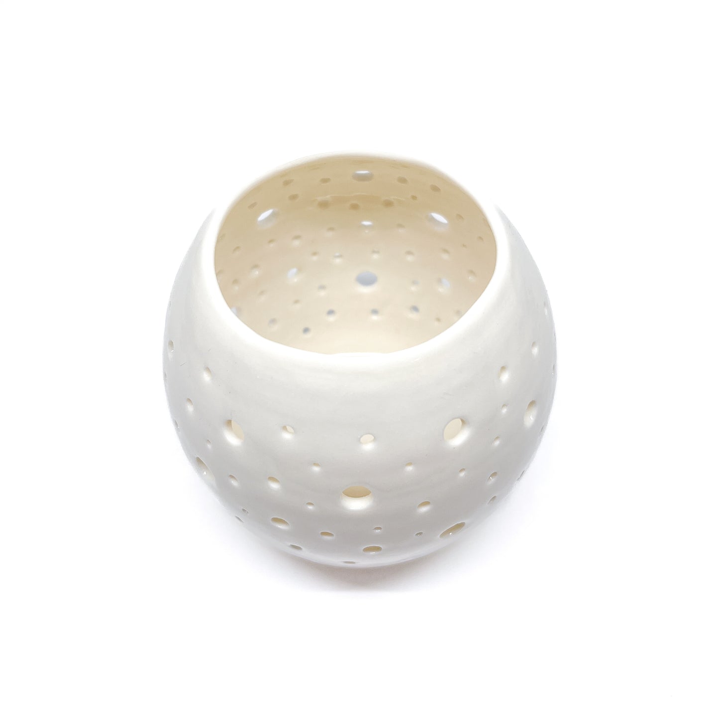 A white ceramic tealight holder with small holes cut out around its surface, seen from above.