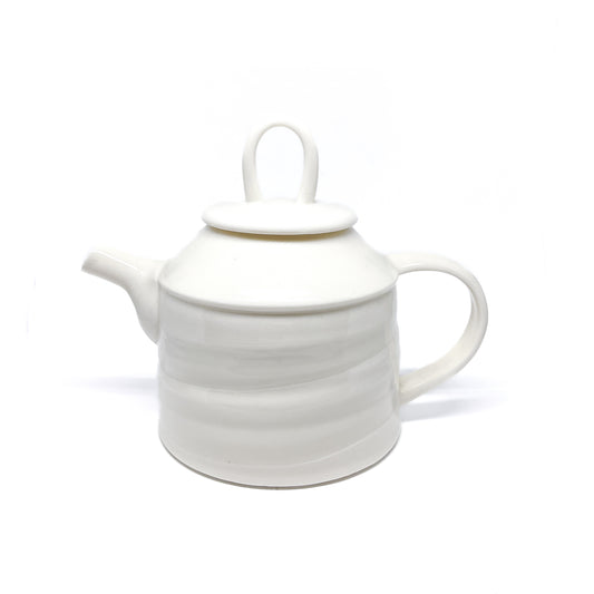 A white ceramic teapot with a lid, spout, and handle, featuring horizontal ridges around the body.