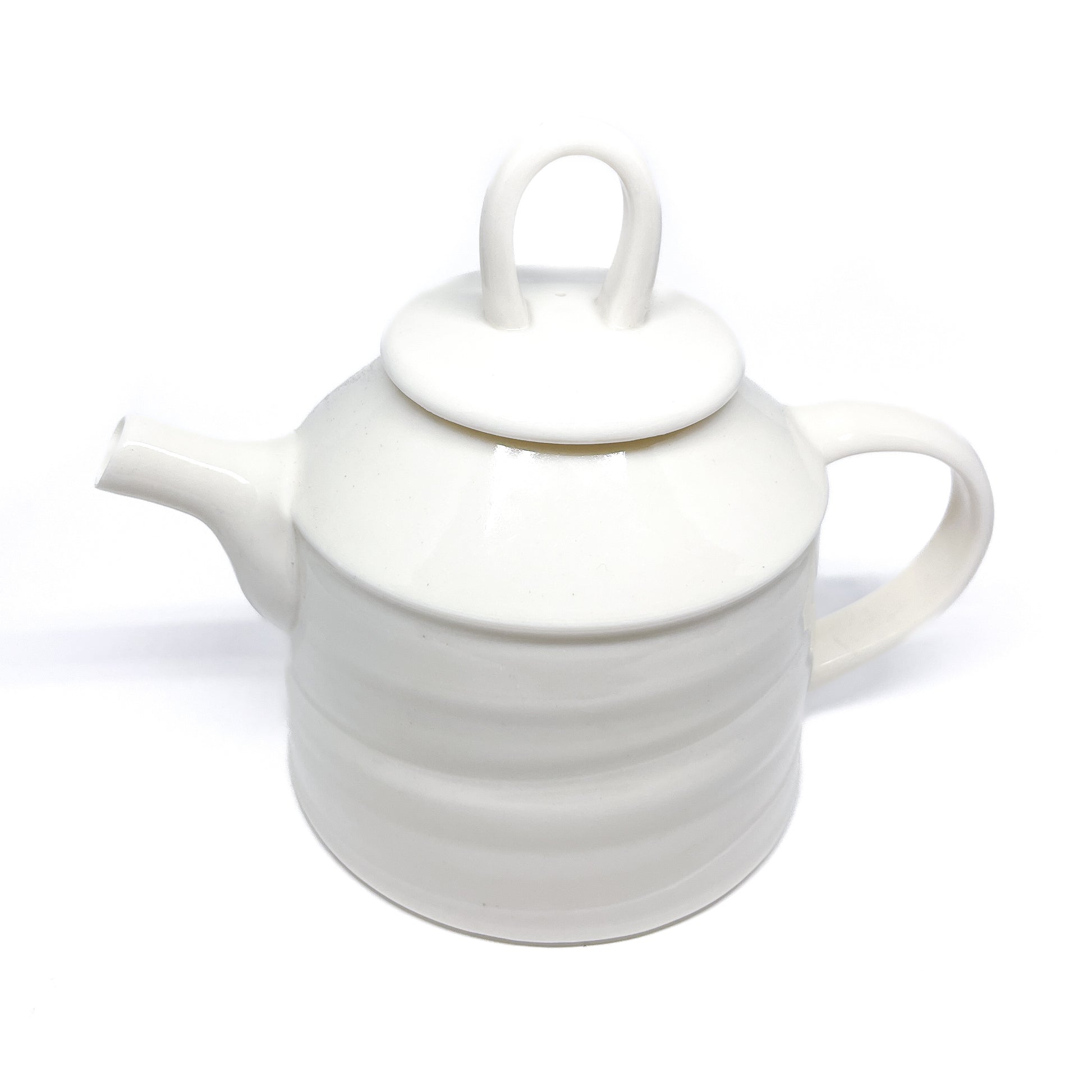 A white ceramic teapot with a lid, spout, and handle, featuring horizontal ridges around the body, seen from above.