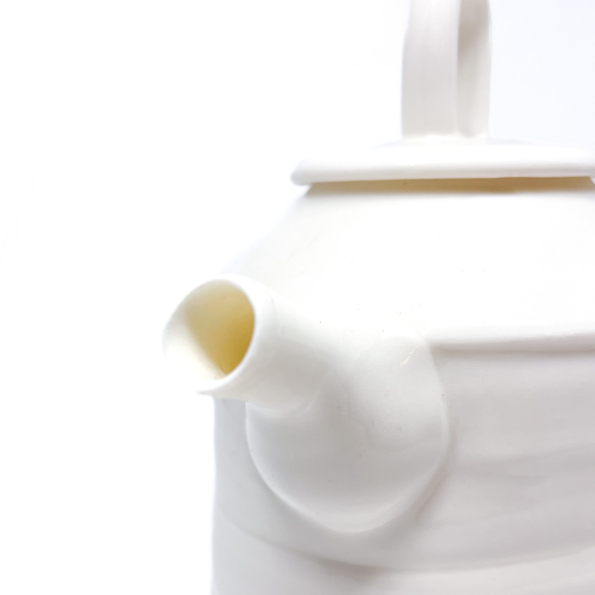 A close-up of the spout of a white ceramic teapot, showing the smooth texture and design.