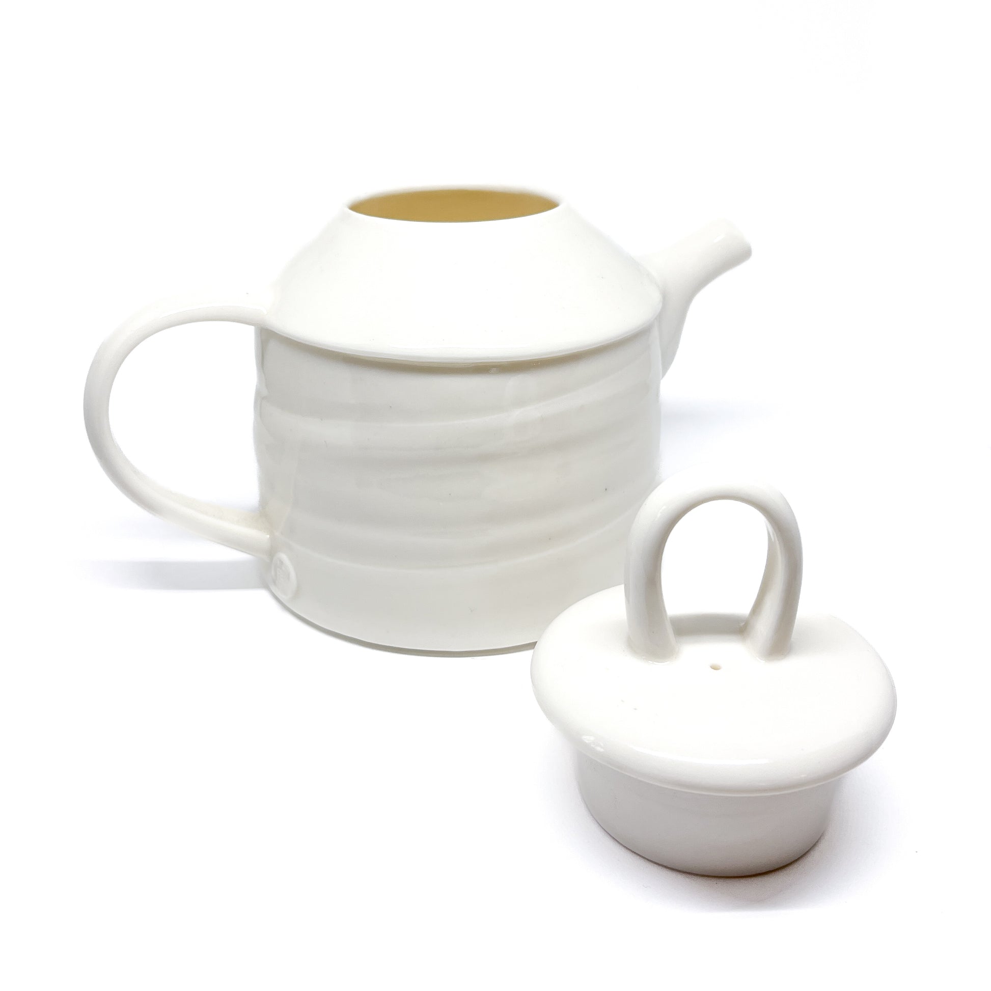 A white ceramic teapot with the lid removed, showing the inside and the separate lid with a loop handle.