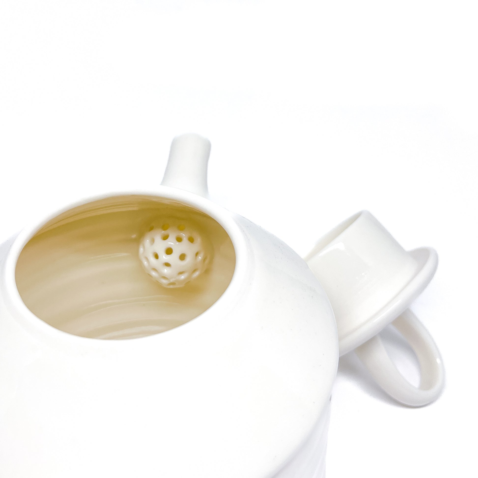 A white ceramic teapot with the lid removed, showing a spherical infuser inside the pot.