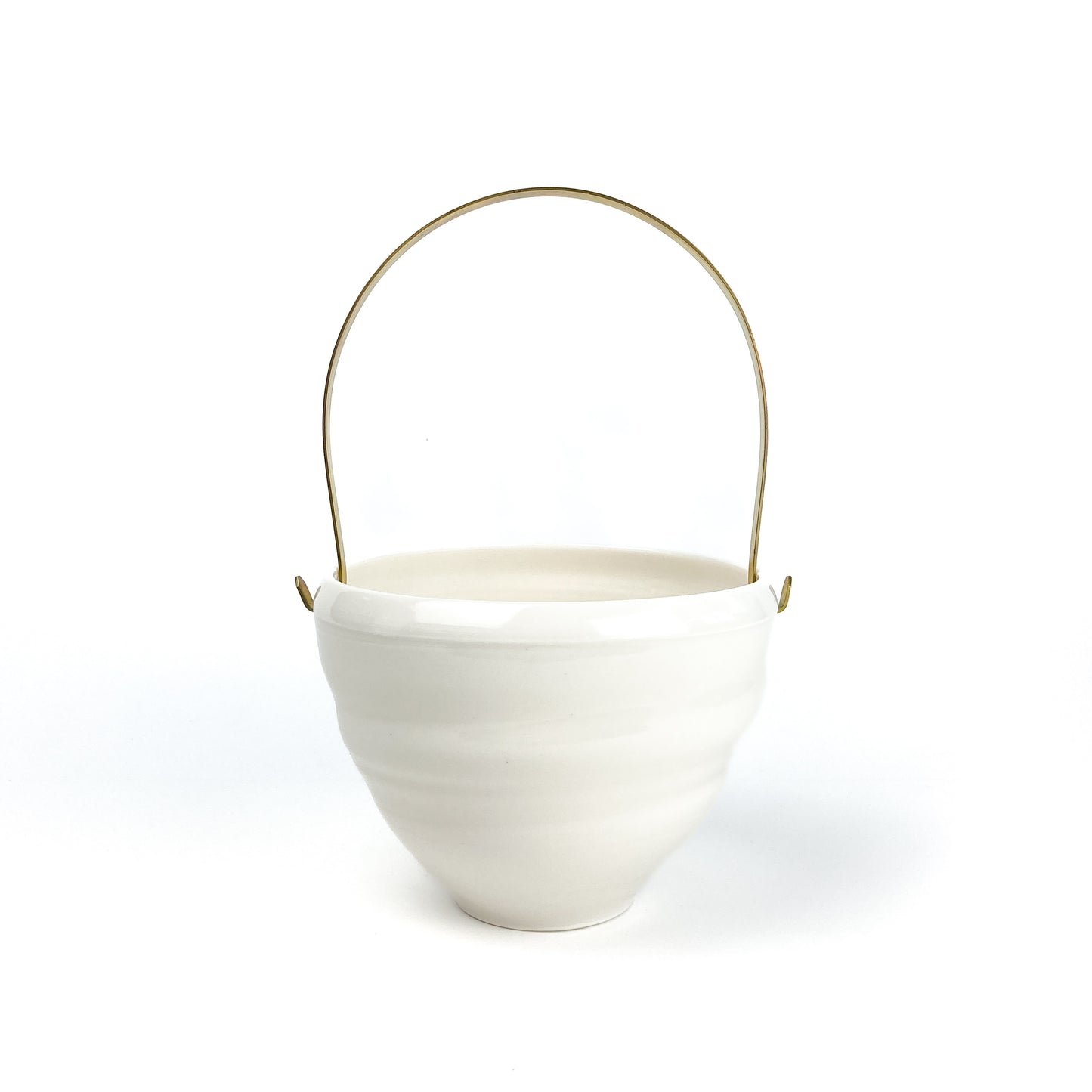 A white ceramic bowl with a brass handle, featuring horizontal ridges around the body.