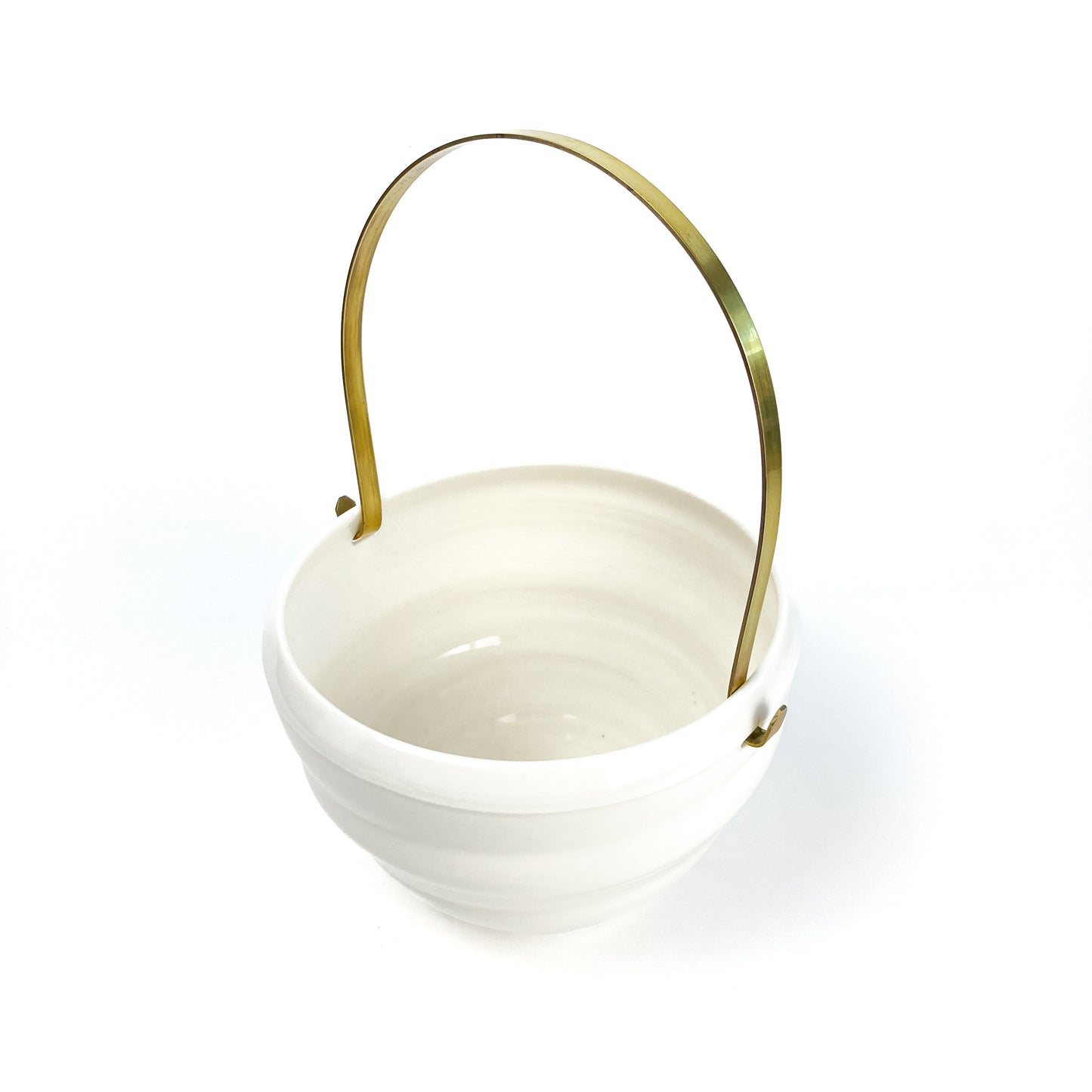 A white ceramic bowl with a brass handle, featuring horizontal ridges around the body, seen from above.