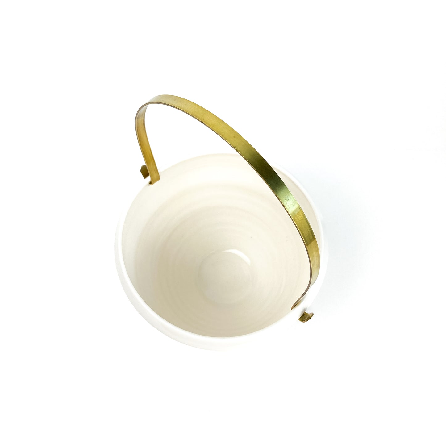 A white ceramic bowl with a brass handle, seen from directly above.