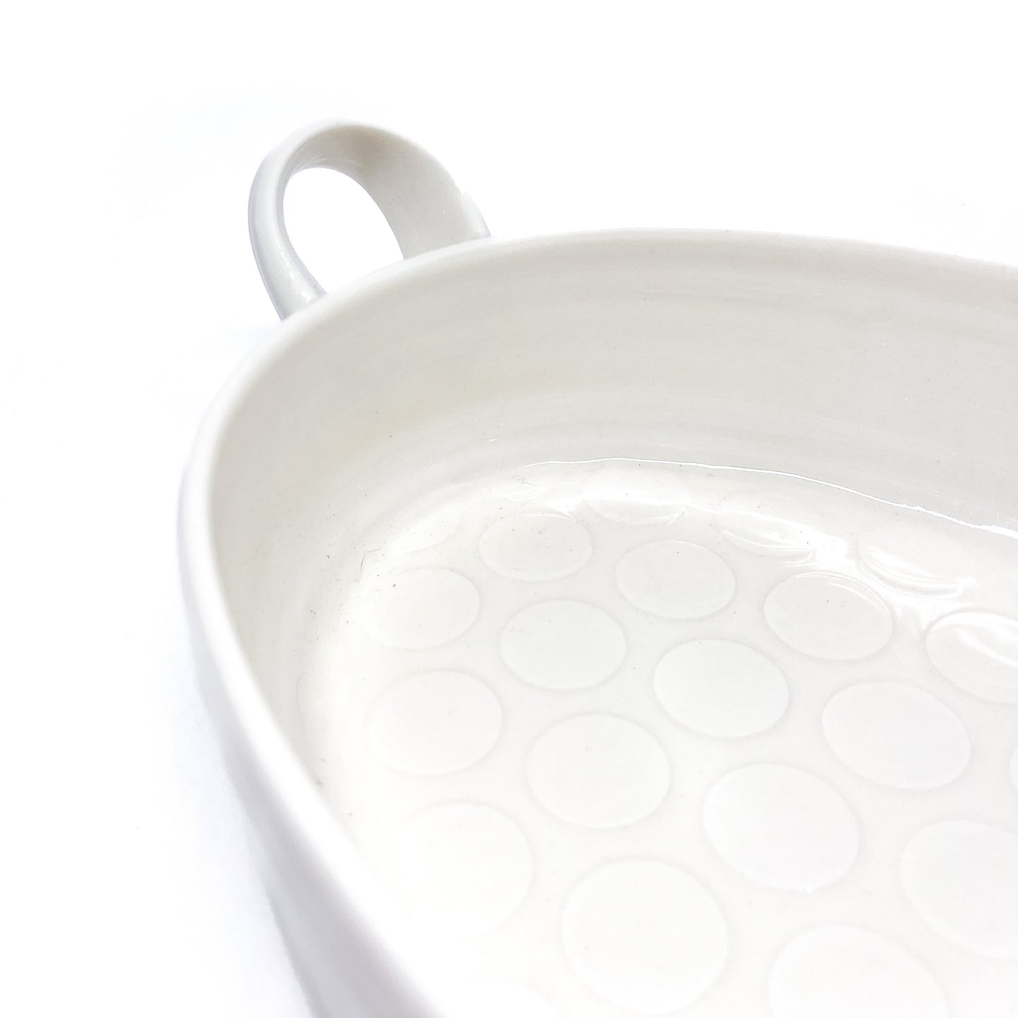 A close-up of the interior of a white oval ceramic casserole dish, showing a pattern of circles on the bottom.