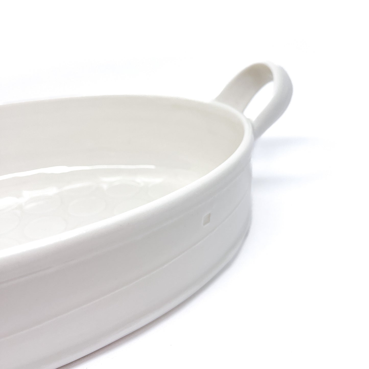 A close-up of the handle and rim of a white oval ceramic casserole dish.