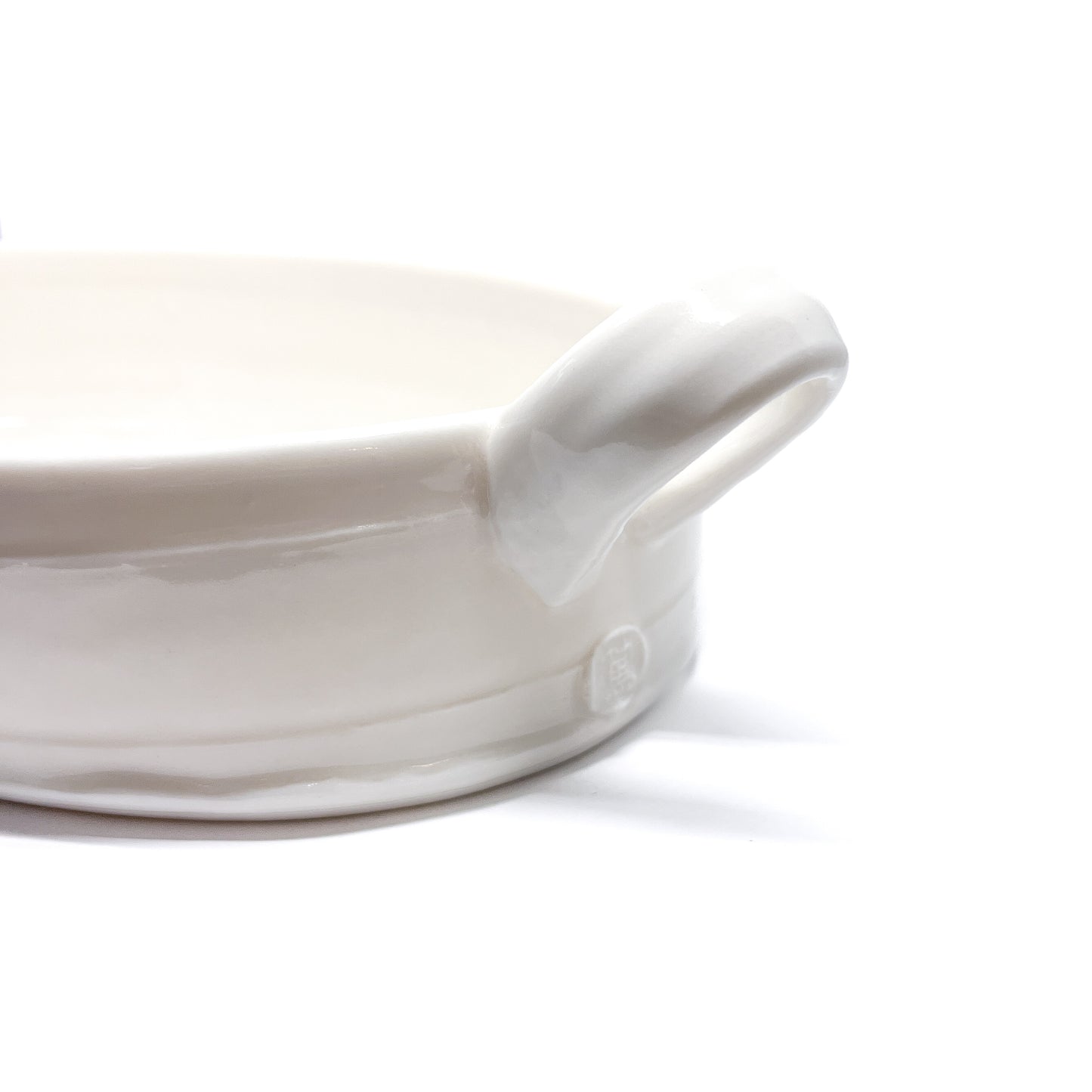 A close-up of the handle and base of a white oval ceramic casserole dish, showing a small circular mark.