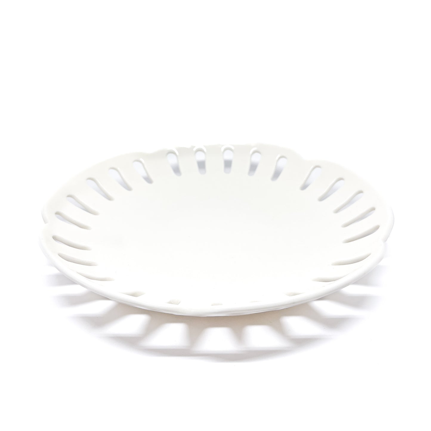 A round, white ceramic plate with decorative cut-outs around the edge.
