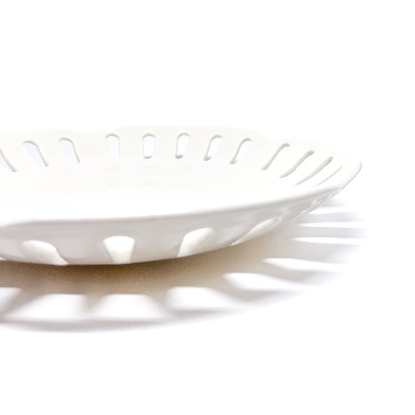 A close-up of a white ceramic plate with decorative cut-outs around the edge, showing the texture and shadow.