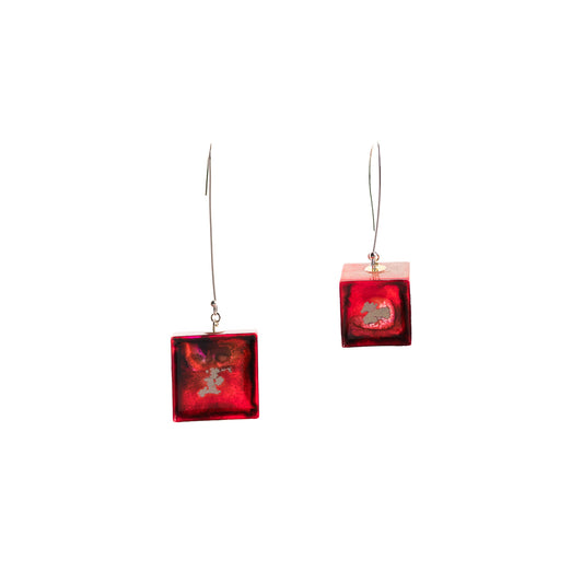 A pair of drop earrings featuring translucent red cubes with embedded abstract metallic elements and silver hooks.