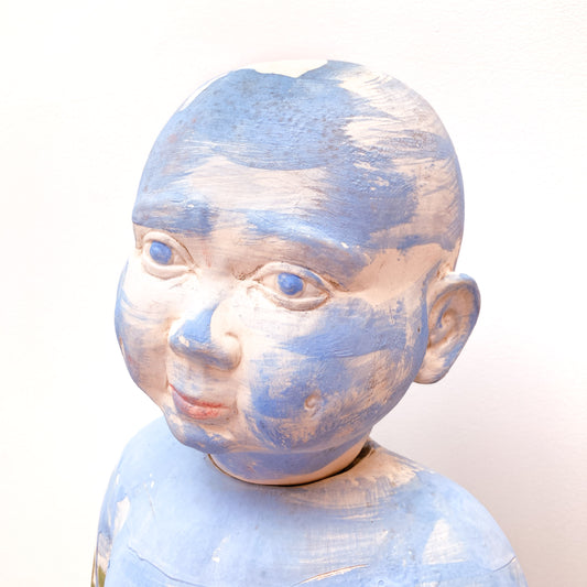 A close-up of a baby sculpture head with blue paint on its face and torso.