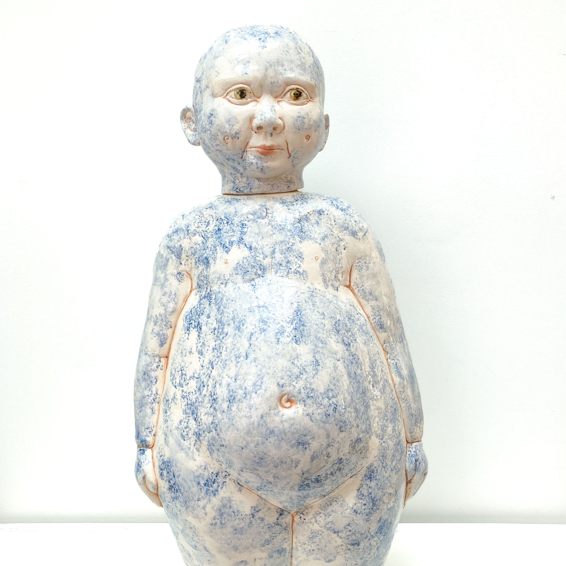 A full shot of a baby sculpture with blue paint on its face and body.