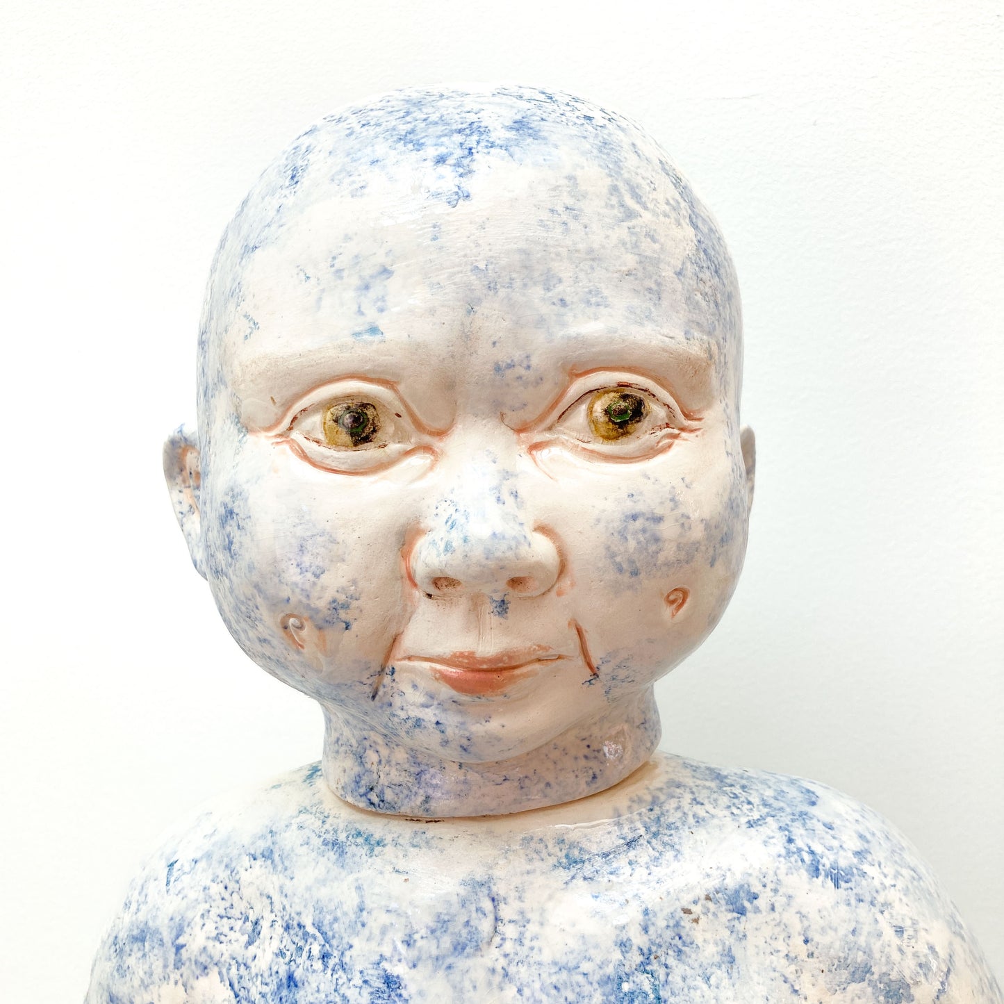 A close-up of a baby sculpture head with blue paint on the face.