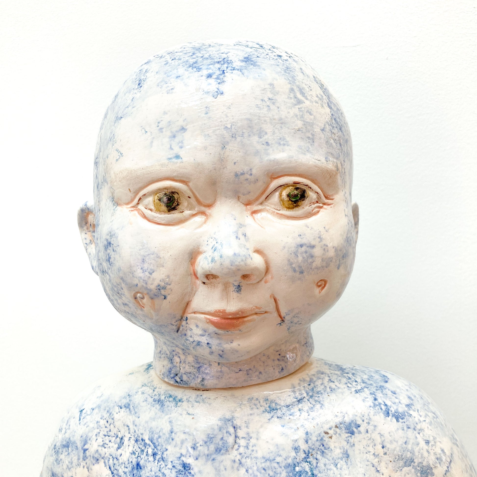 A close-up of a baby sculpture head with blue paint on the face.