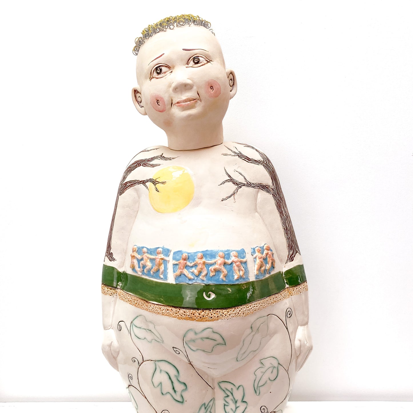 A baby sculpture with a bald head, painted eyes, and metal rings for hair, with additional designs on its body.