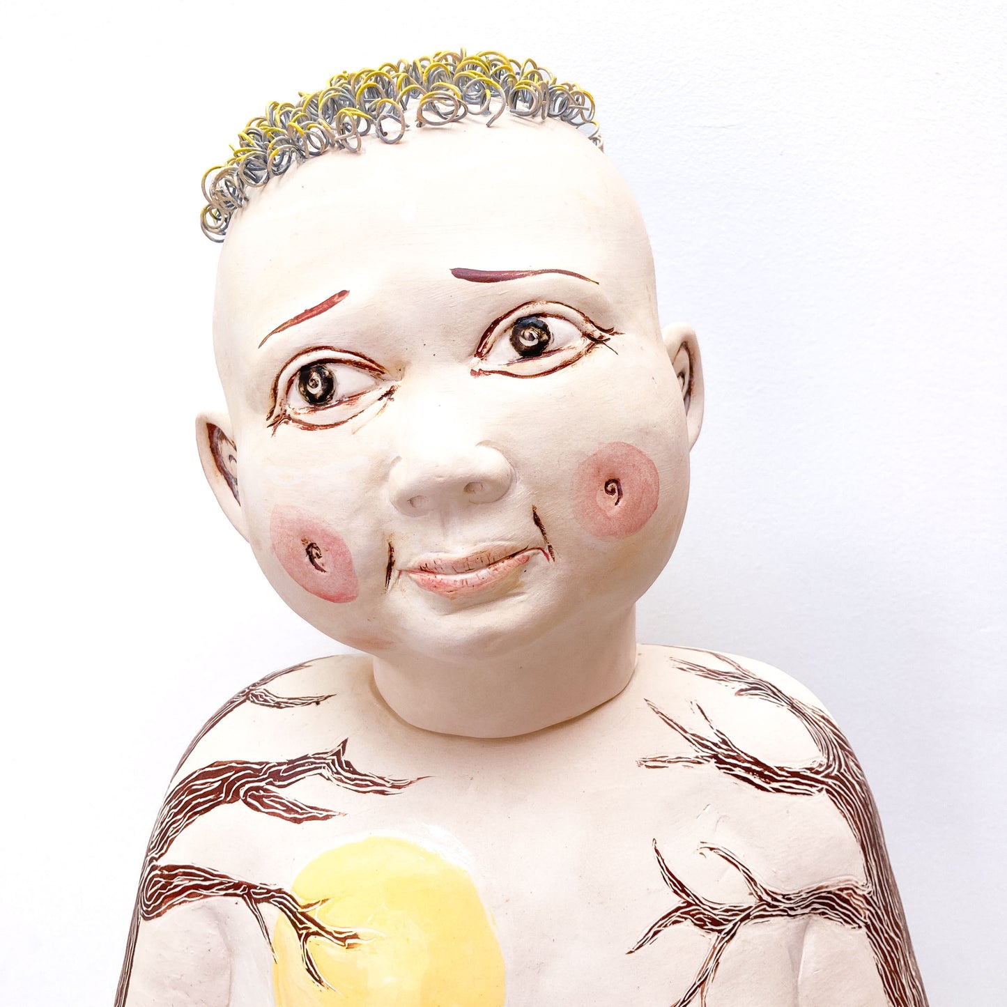 A baby sculpture with a bald head, painted eyes, and metal rings for hair.