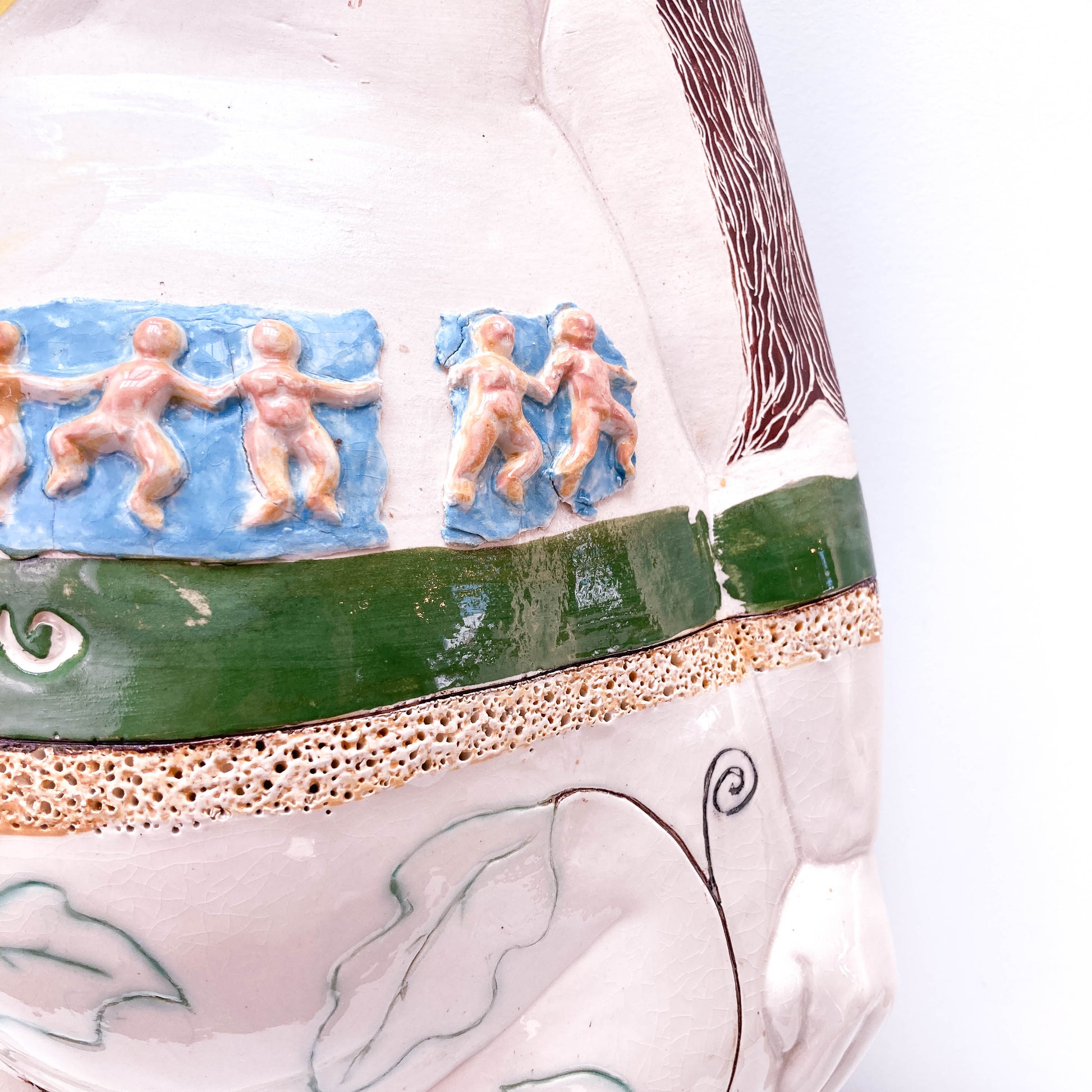 A close-up of a baby sculpture's body with relief carvings of small figures and a decorative border.