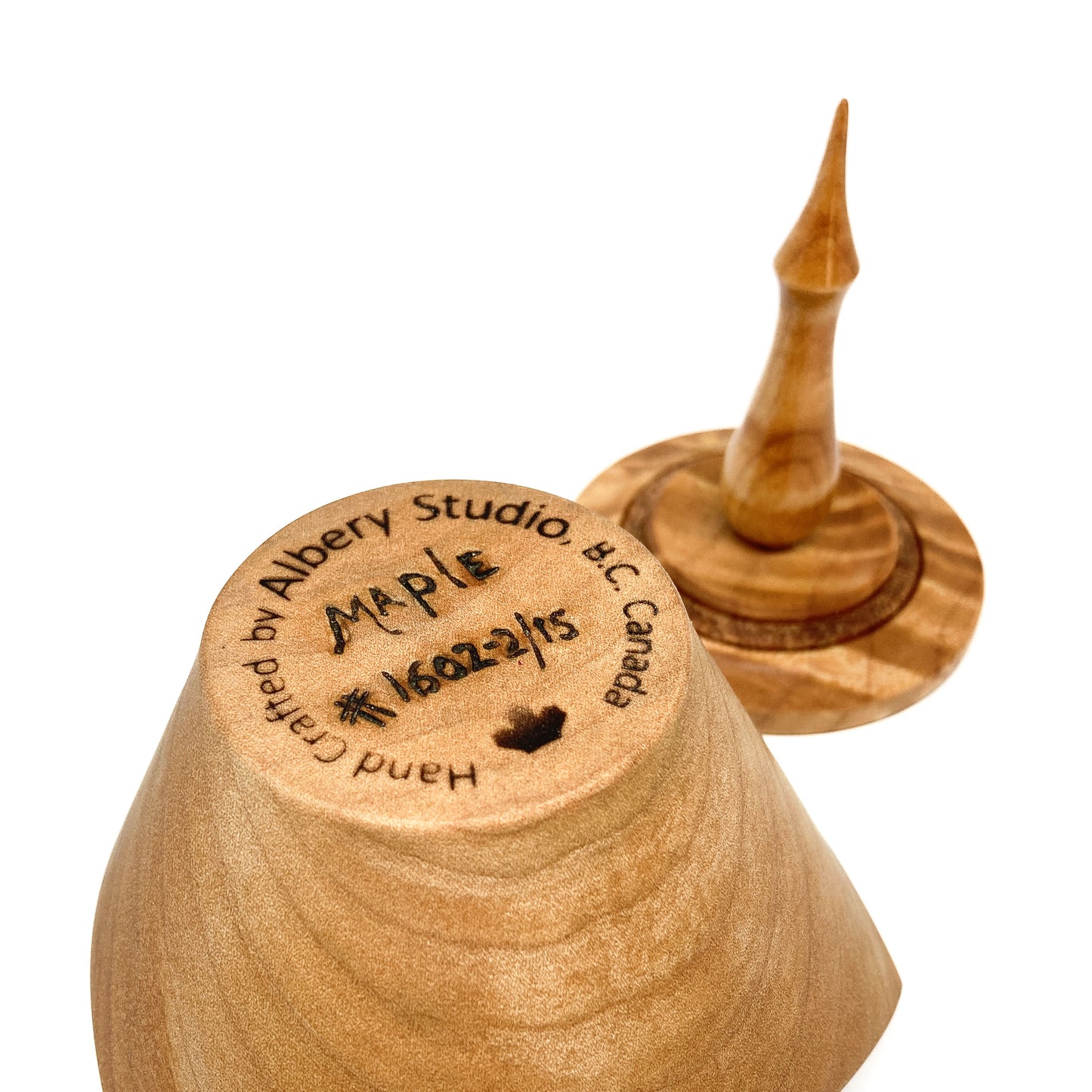 A turned wooden box lid with a pointed finial, showing the maker's mark on the bottom.