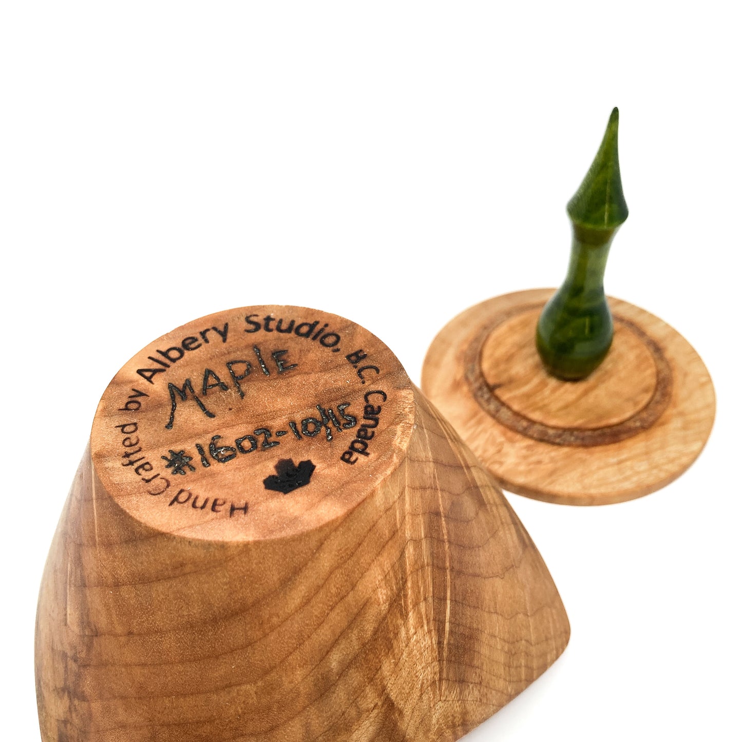 A turned wooden box lid with a pointed green finial, showing the maker's mark on the bottom.