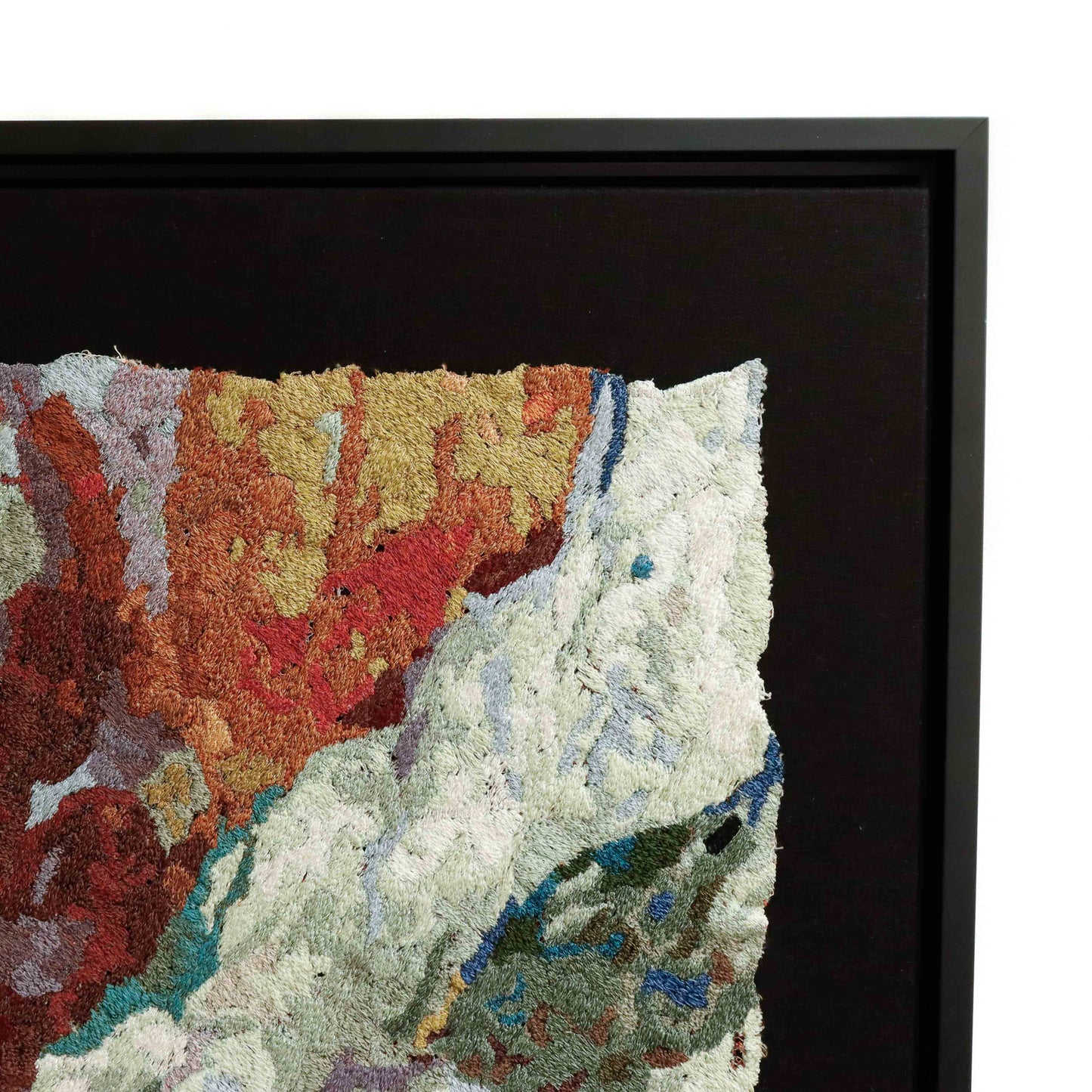 Close-up of a framed thread painting, showcasing intricate stitching and colorful thread in an abstract embroidery design.