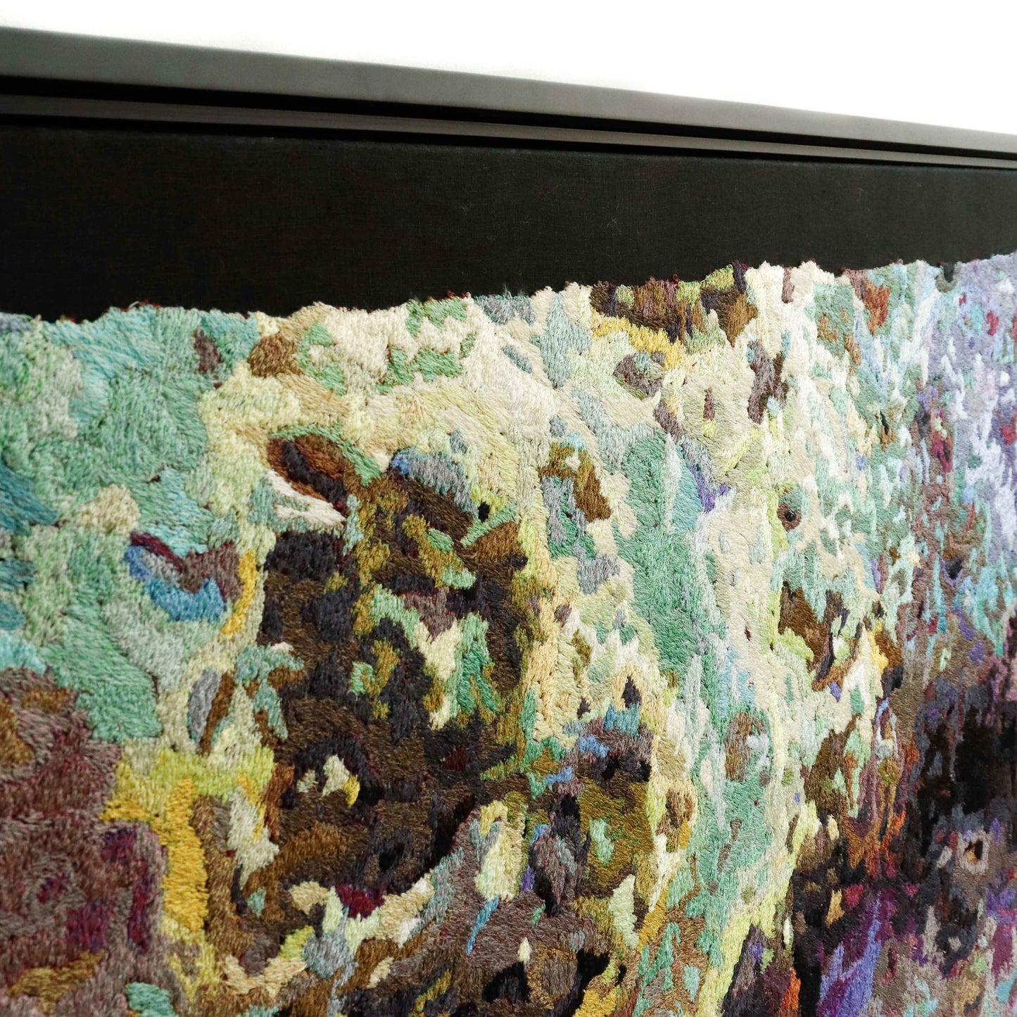 Angled view of a framed thread painting, showcasing dense, colorful thread stitching in an abstract design.