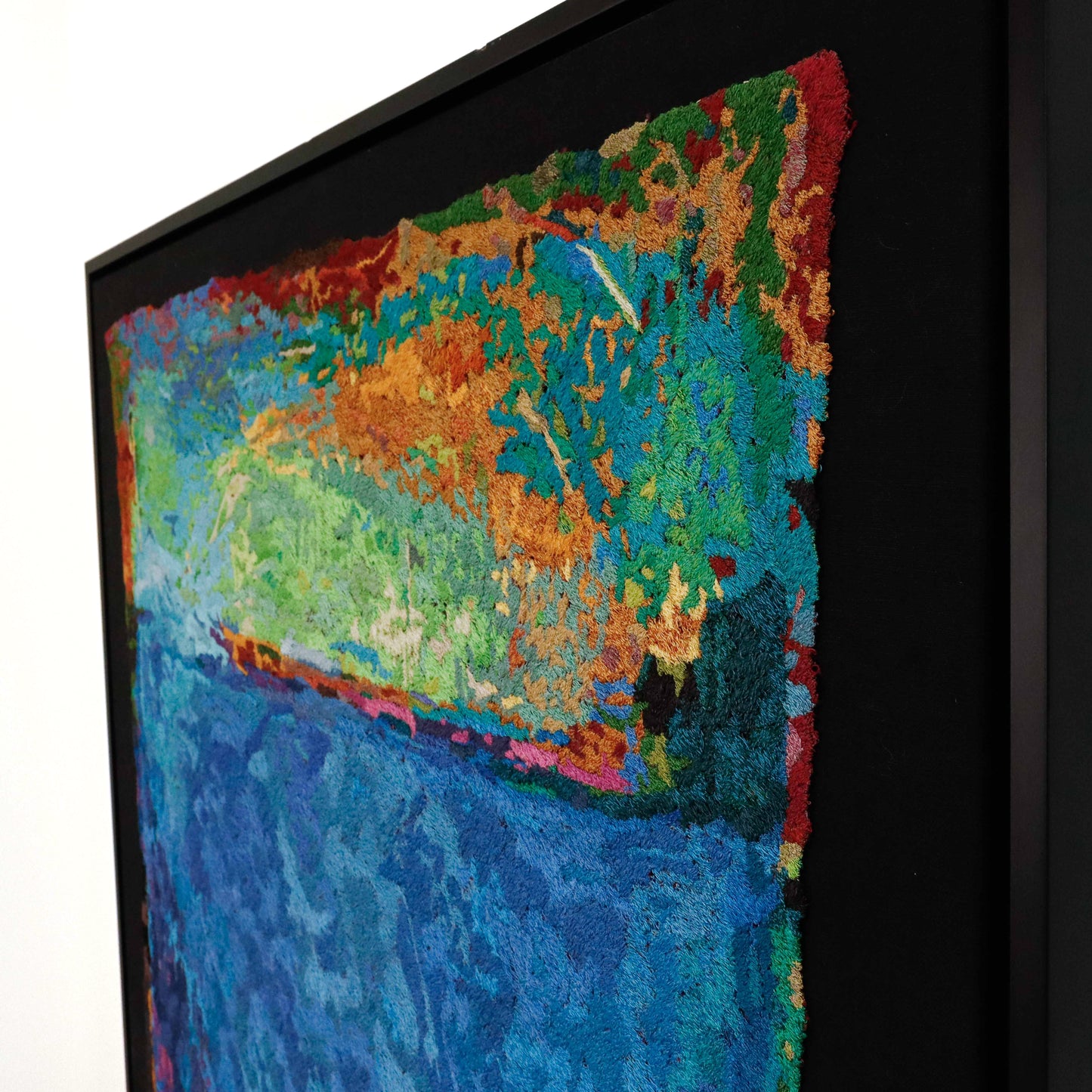 A framed thread painting, angled view, displaying intricate stitching and colorful thread in a landscape thread painting.