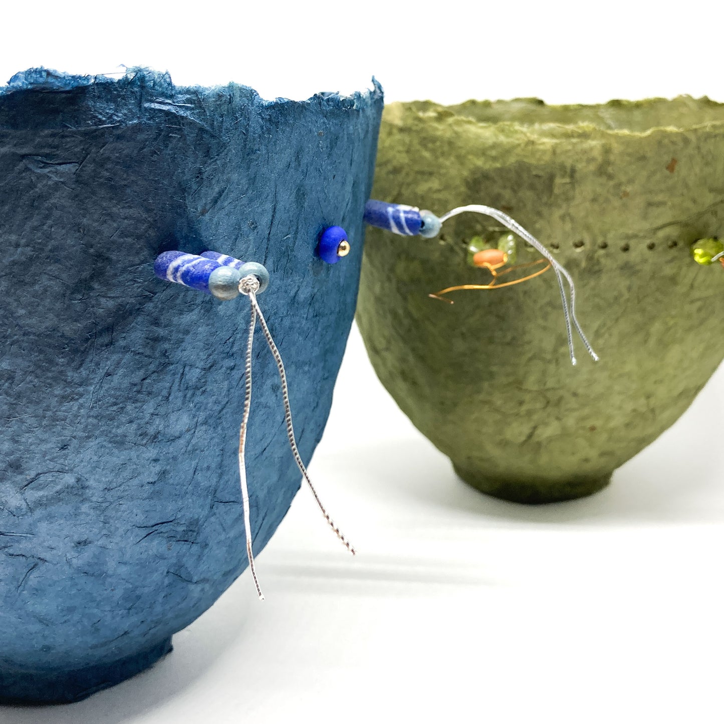 A close-up shows a blue and a green textured plant paper bowl, each with unique wire and bead decorations.