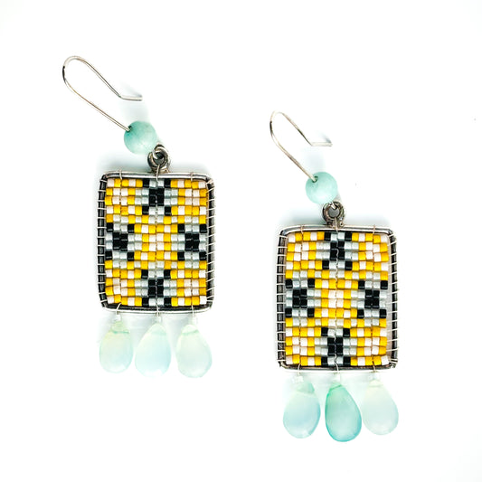 Two rectangular dangle earrings feature a yellow, white, and black beaded pattern with pale blue teardrop charms and beads.