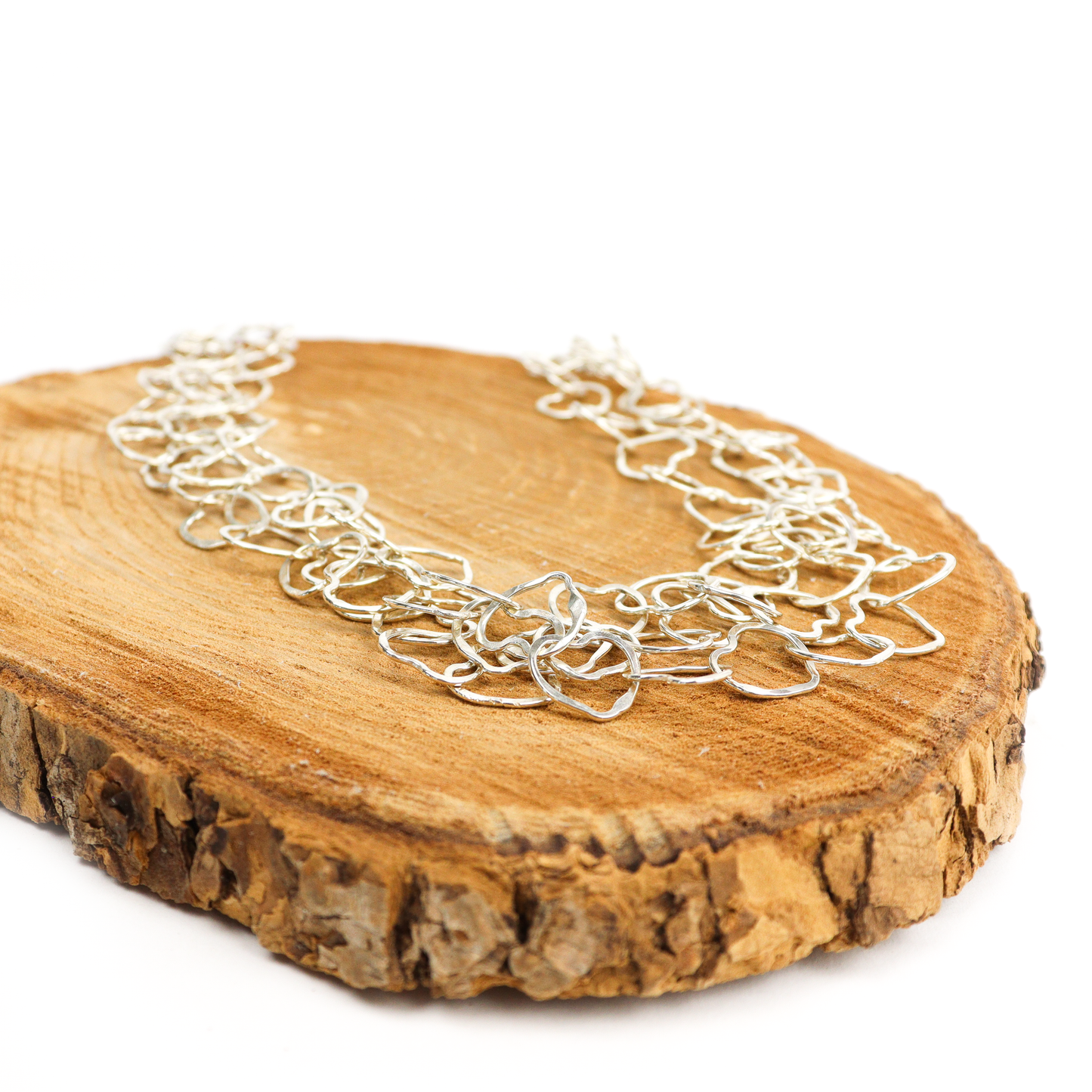 Heart Necklace displayed on a wooden surface, showcasing layered silver hearts linked together.