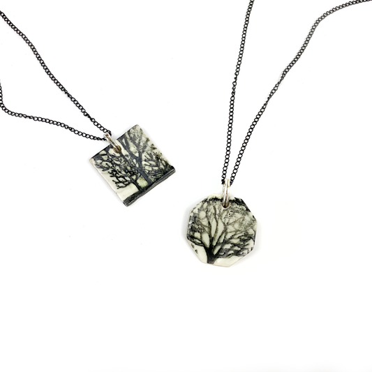 Two necklaces on a white surface, one square and one round, each with a tree design on a pendant.