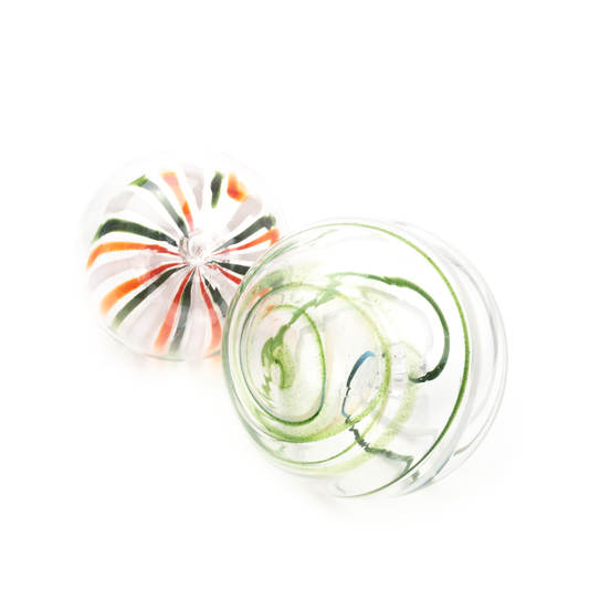 Two round glass swirl ornaments. One has red, white, and green radiating lines, the other has green and blue spiral lines.