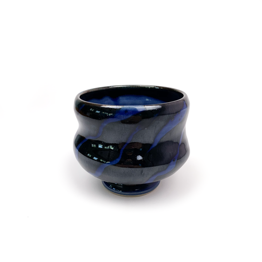 A dark ceramic tea bowl with blue swirls, resting on a small pedestal.