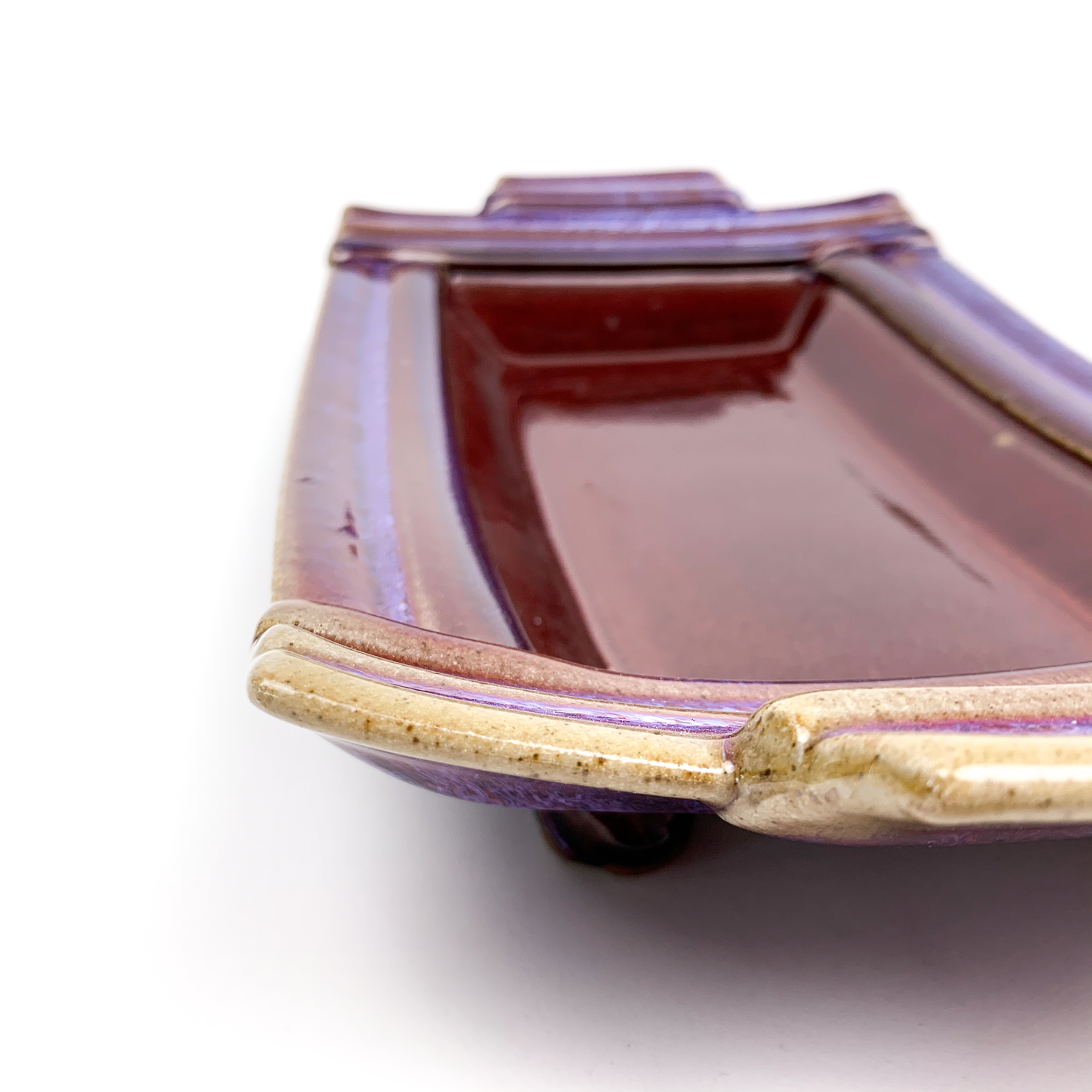 A close-up of a square, ceramic bonsai pot with a glossy purple glaze and small feet.