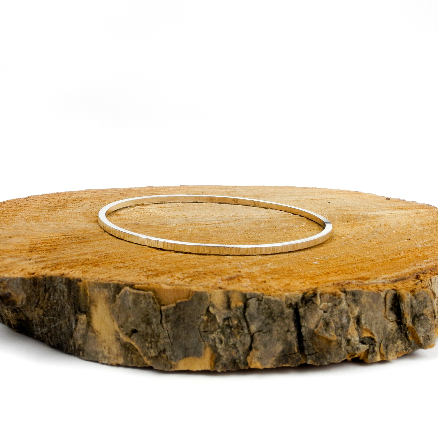 A thin, textured, metallic bangle rests on a piece of wood.
