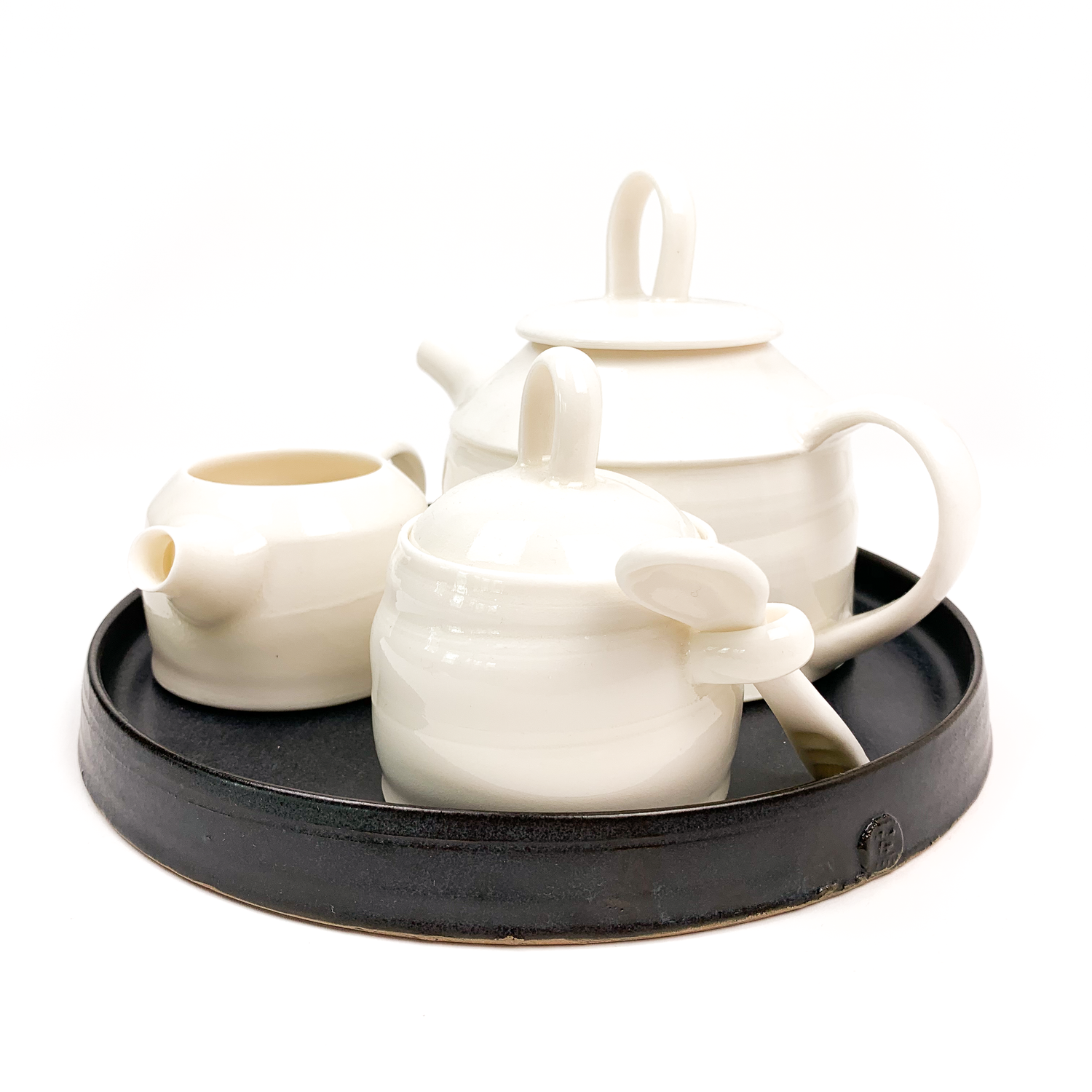 A white ceramic tea set with a teapot, creamer, and sugar bowl on a black tray.