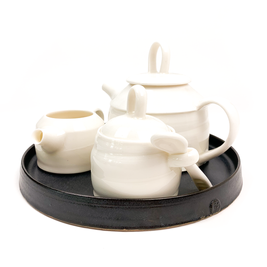 A white ceramic tea set with a teapot, creamer, and sugar bowl on a black tray.