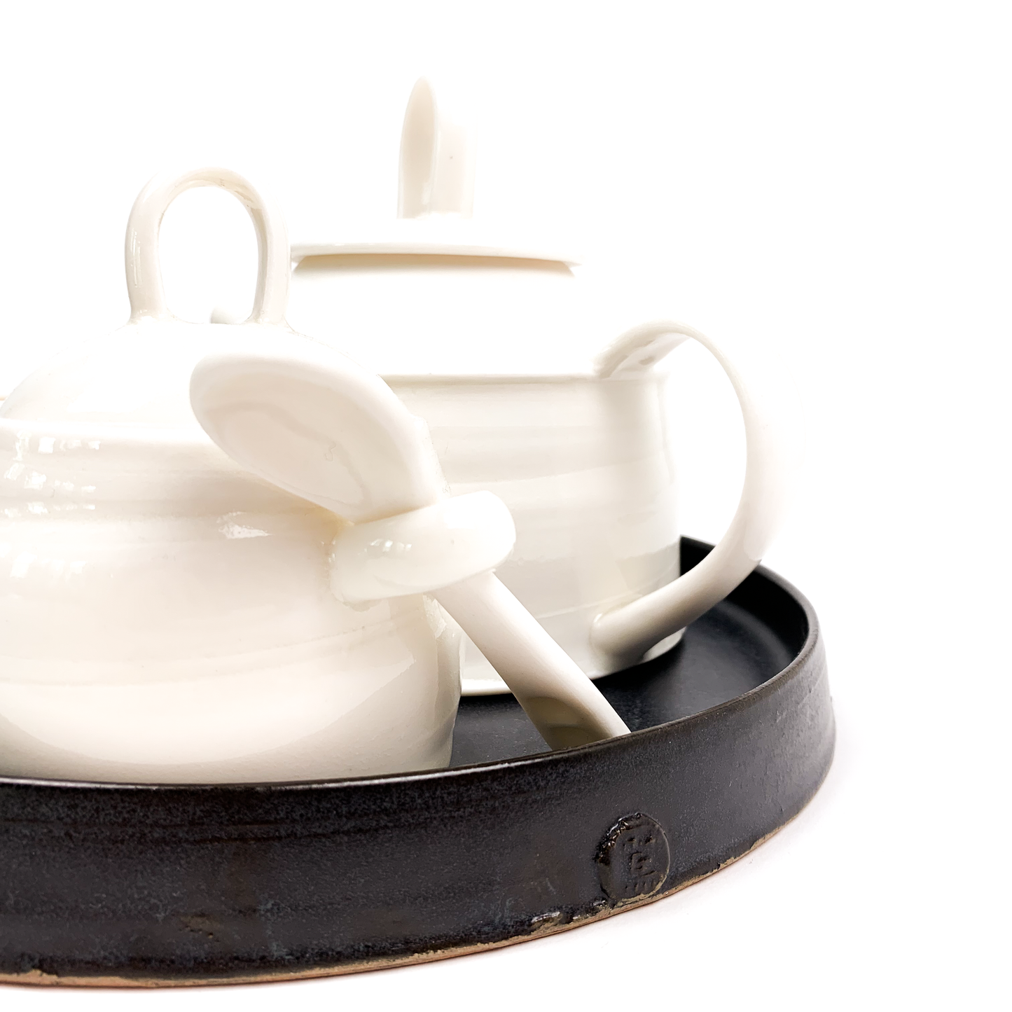 A close-up of a white ceramic sugar bowl with a spoon on a black tray, part of a tea set.
