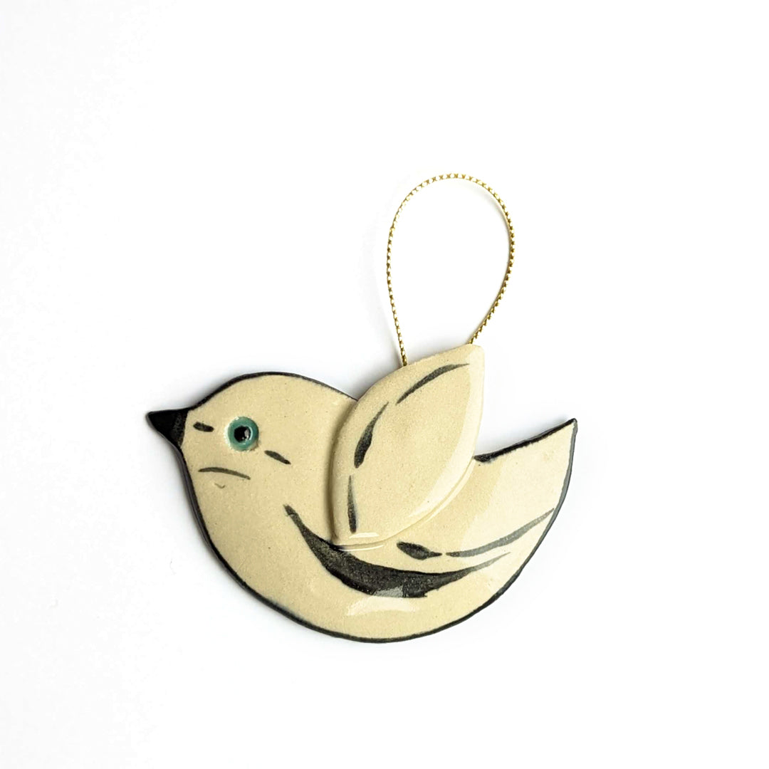 A cream-colored bird ornament with black accents, a teal eye, and a gold string.