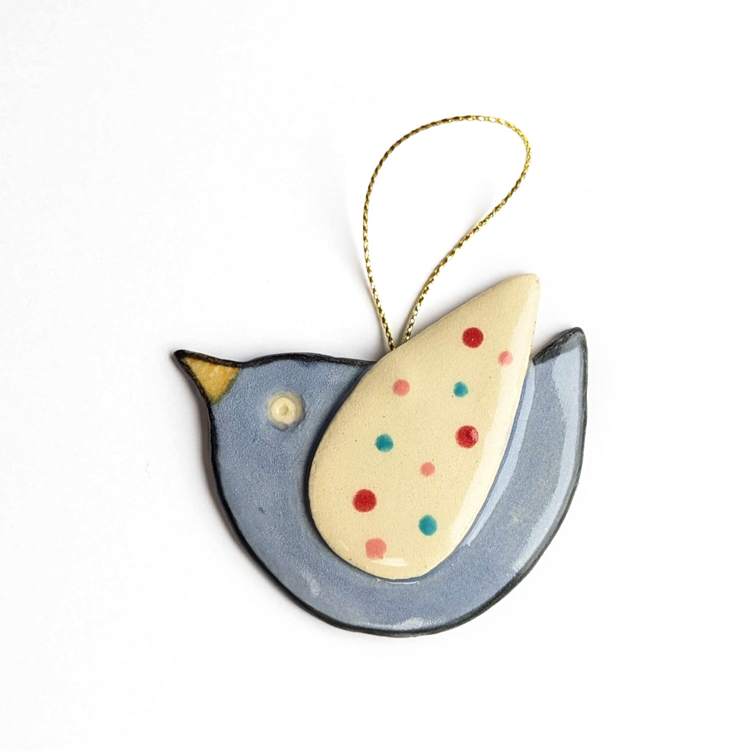 A light blue bird ornament with a cream-colored wing, colorful dots, and a gold string.