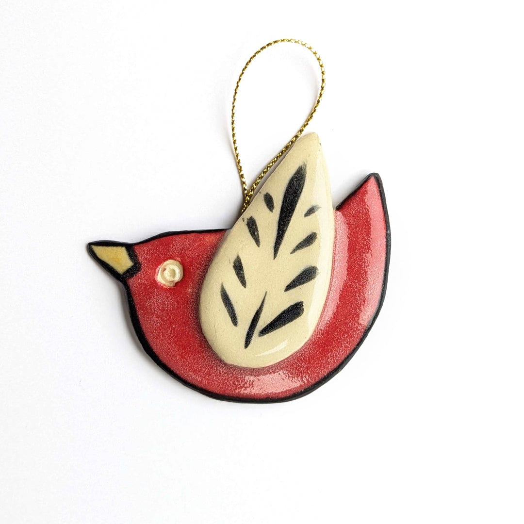 A red bird ornament with a cream-colored wing, black leaf-like pattern, and a gold string.
