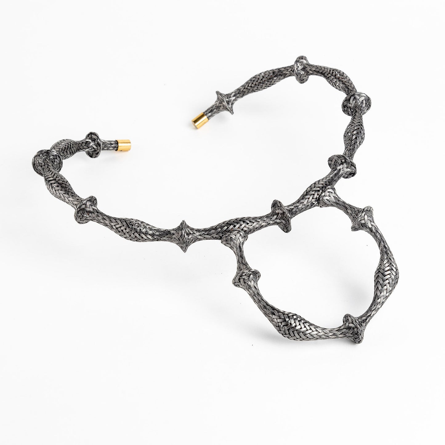 Braided stainless steel cuff bracelet with gold end caps, curved in a heart shape, on white.