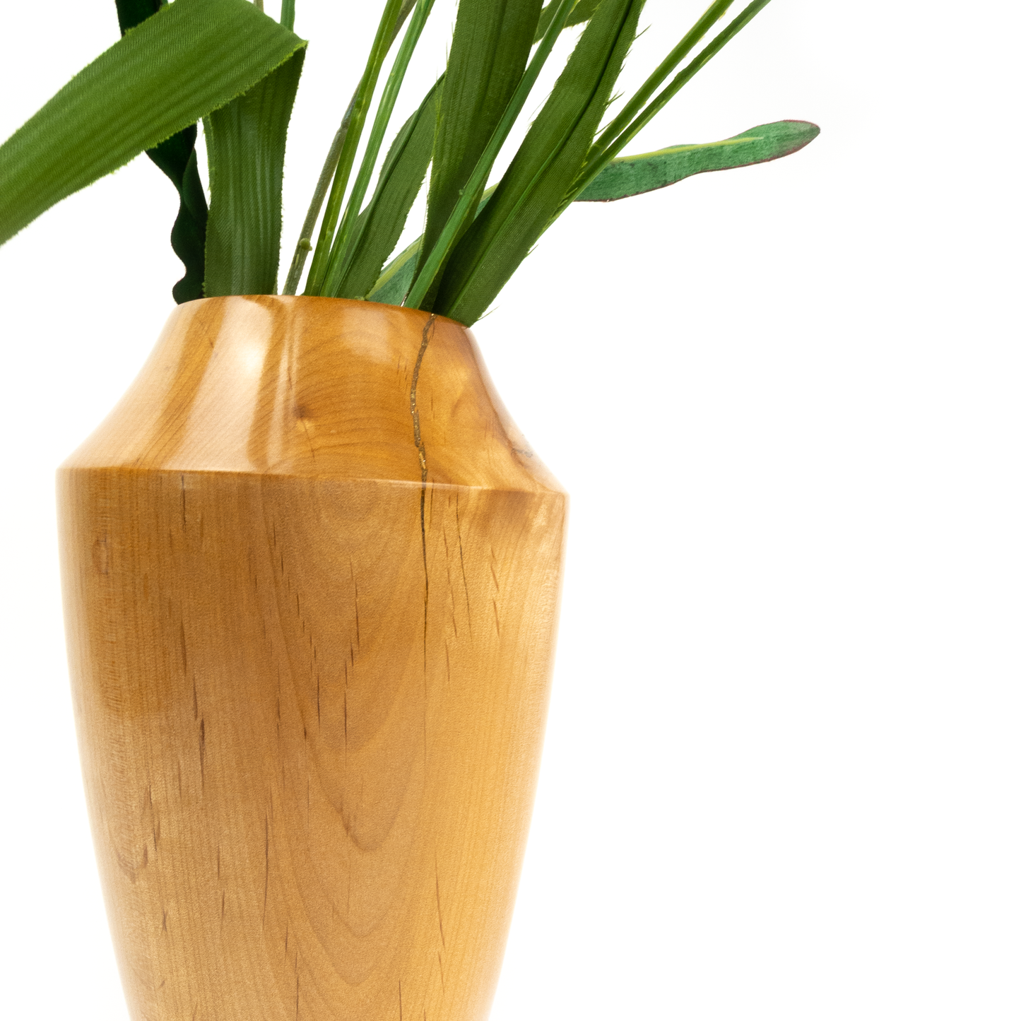 Close-up of a light brown wooden vase with green leaves.