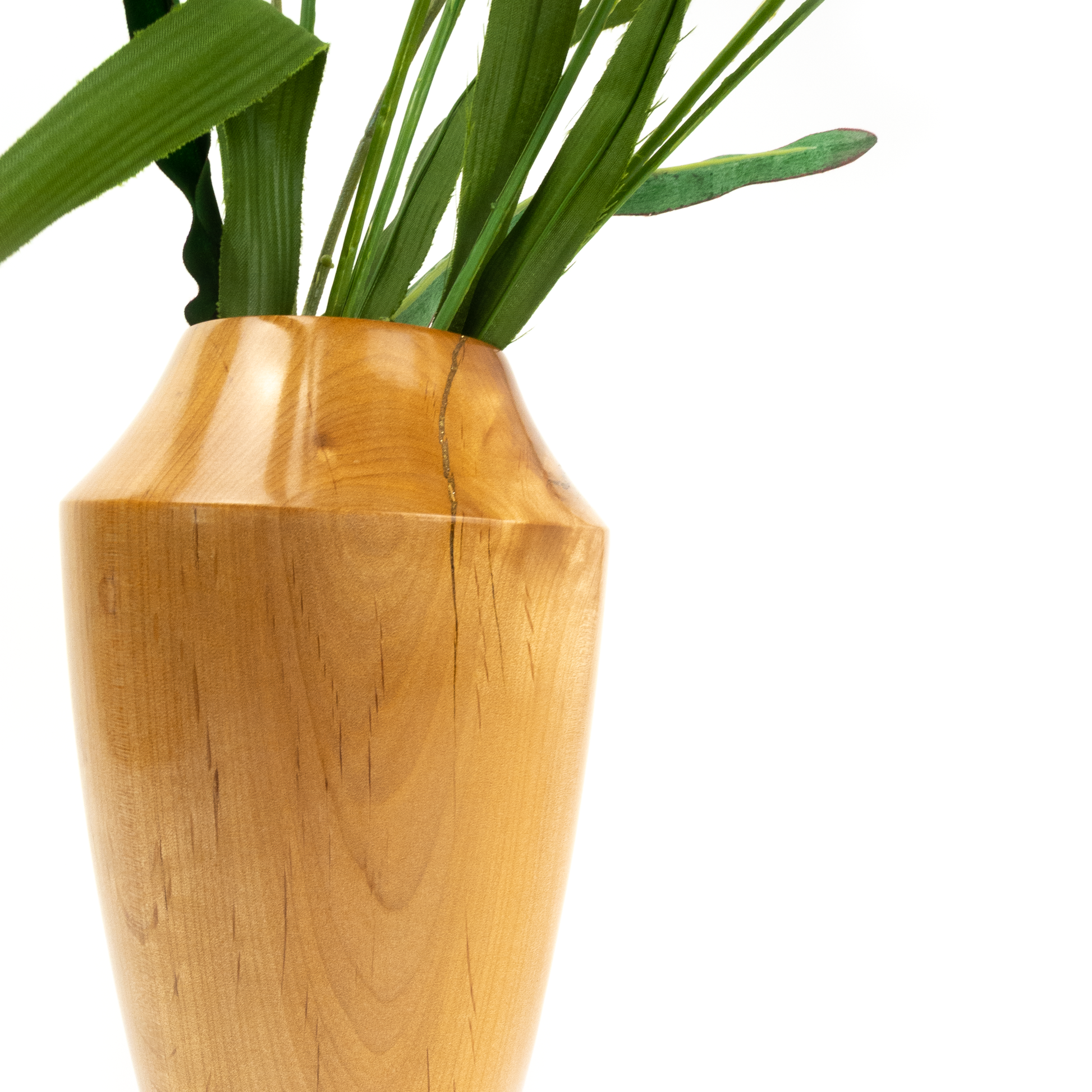 Close-up of a light brown wooden vase with green leaves.