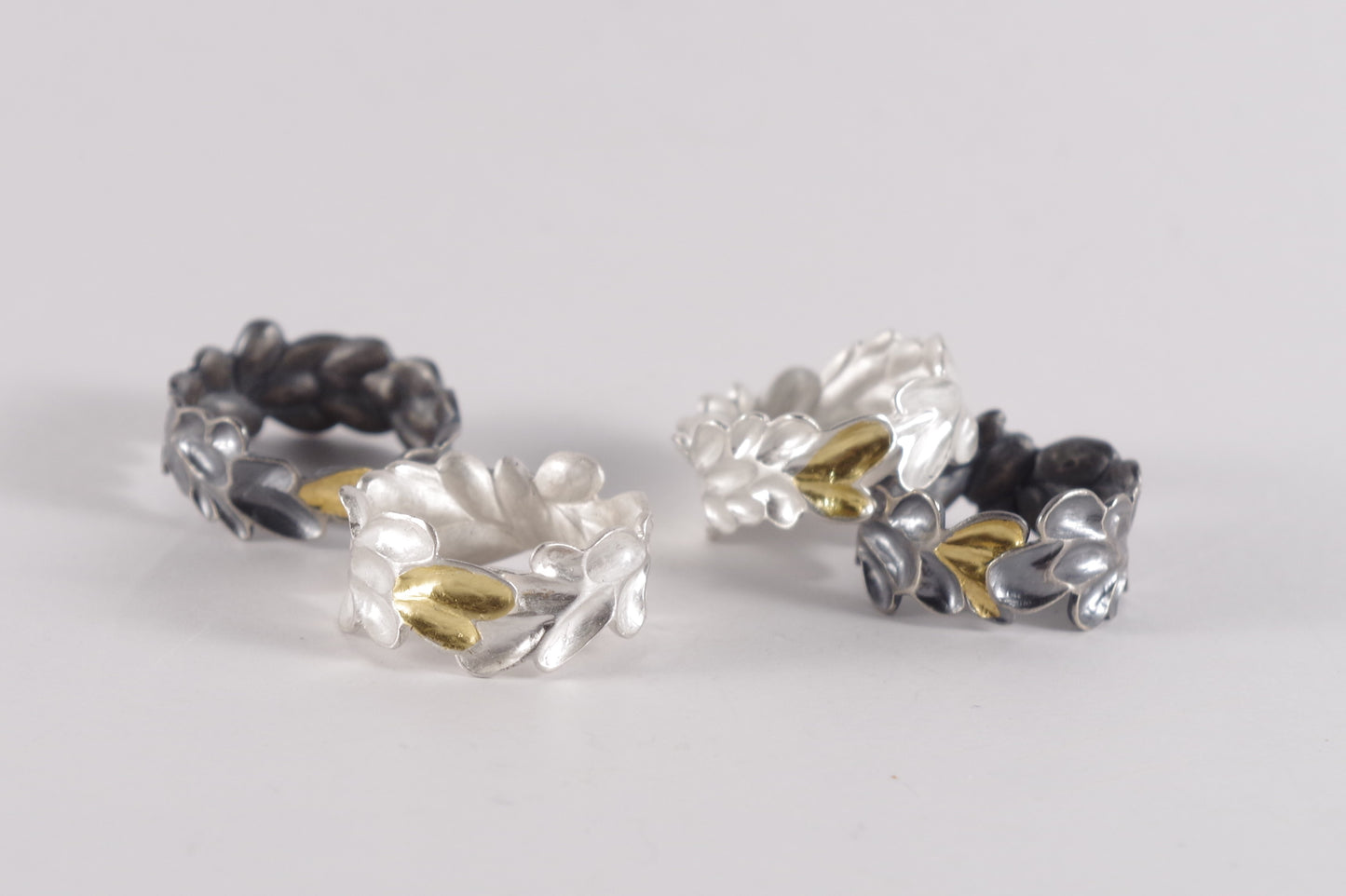 Four sterling silver and Keum-Boo rings with textured, abstract floral or leaf-like designs and contrasting gold accents.