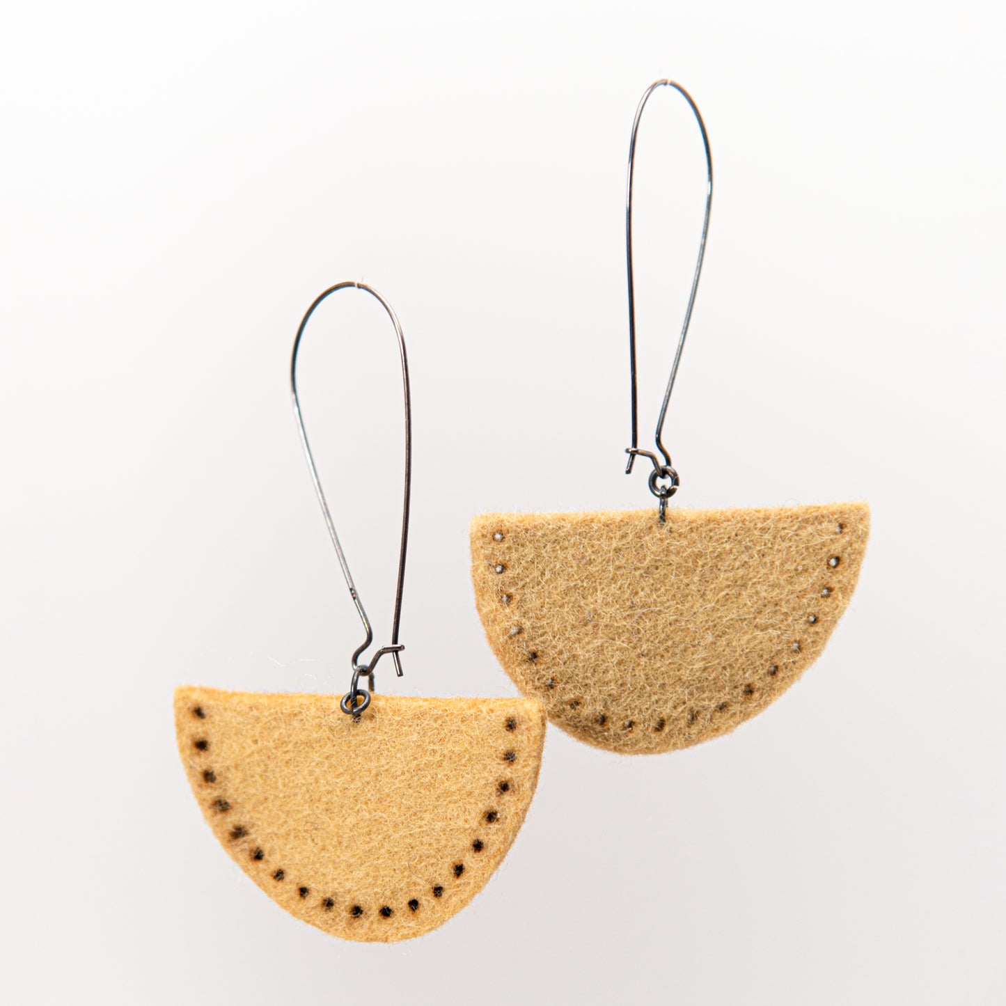 Two tan semi-circular earrings with small dark accents hang from silver hooks.